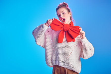 Portrait of an excited pretty girl in a white sweater and with a big elegant red bow on her neck...