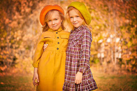 Autumn season. Two cute little girls walk through a beautiful autumn park. Retro style. Children's fashion.の写真素材