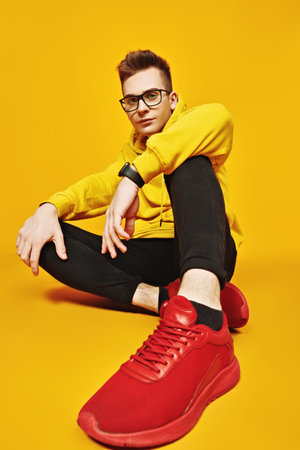 Cool young man in bright yellow hoody and glasses posing on a yellow background. Youth fashion.