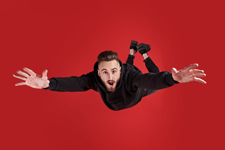 Excited young man is flying through the air like a . Studio portrait on a red background.
