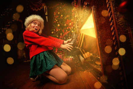 Funny mischievous girl pulls Santa out of the fireplace by his boots at home. Merry Christmas and Happy New Year!の写真素材