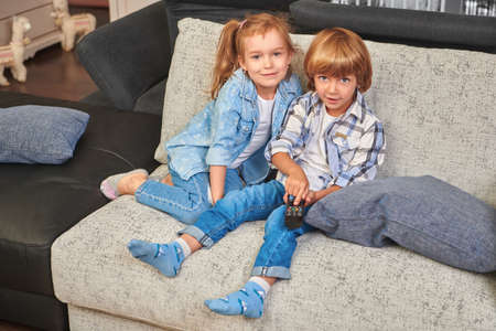 Happy little brother and sister watch TV, holding a remote control. family life at home. Happy childhood. Family at home.の写真素材