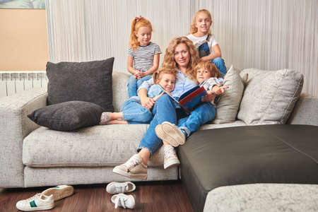 A mother reads a book to children on sofa in a living room at home. Happy family at home.の写真素材