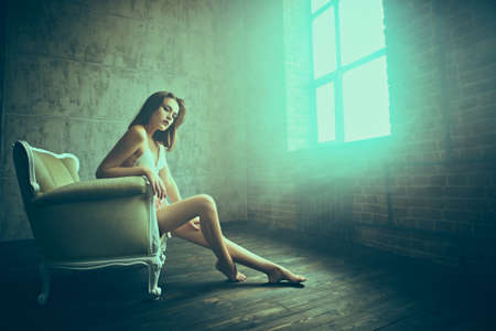 Beautiful tender girl in white lingerie sits in a classic vintage armchair. Beauty, fashion.の写真素材