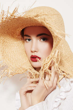 Close up portrait of a beautiful romantic girl in a white blouse and straw hat. Summer season. Beauty and cosmetics.の写真素材