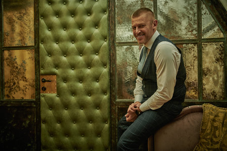 Portrait of a handsome mature man in an elegant classic suit sitting near the door in a luxury...
