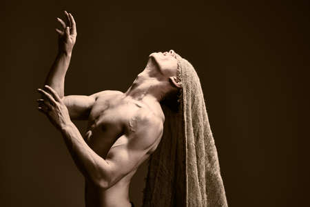Art portrait of a courageous muscular man with burlap on his face, looking up to the light. Studio shot on a black background.の写真素材