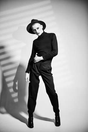 Black-and-white portrait of a young man with women's makeup and in women's clothing posing at studio with expression. Avant-garde fashion.の写真素材
