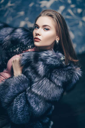 Beautiful fashionable woman posing in a luxurious fur coat in a vintage armchair. Studio fashion shot.の写真素材