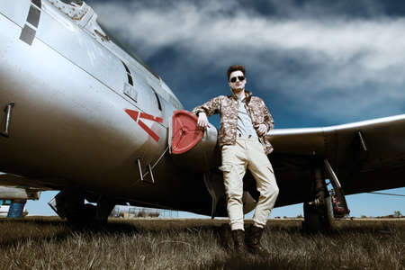 Handsome man pilot wearing military uniform stands by his fighter jet at the airfield. Military aircraft.の写真素材