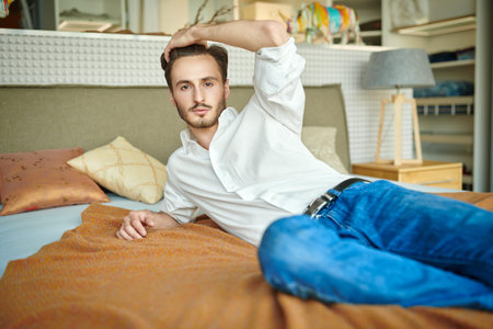 Handsome young man having a rest on the bed in the bedroom at home. Home interior, furniture.