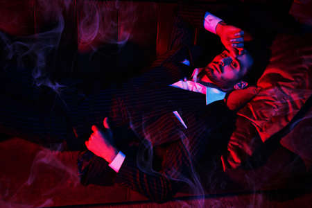 Portrait of a handsome brunet man lying on a sofa in a luxury apartment. Glamorous lifestyle. Fashion shot. Men's clothing and accessories.の写真素材