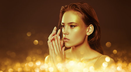 Make-up and cosmetics. Portrait of a gorgeous young woman with golden make-up on a dark background....