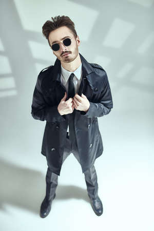 Modern stylish man in elegant black suit, white shirt and sunglasses posing on a gray background with shadows. Full length portrait of a modern businessman. Men's fashion.の写真素材