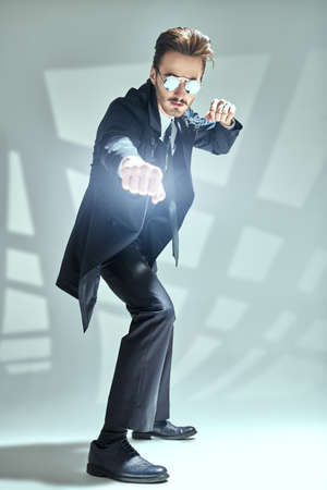 Modern stylish man in elegant black suit, white shirt and sunglasses posing on a gray background with shadows. Full length portrait of a modern businessman. Men's fashion.の写真素材