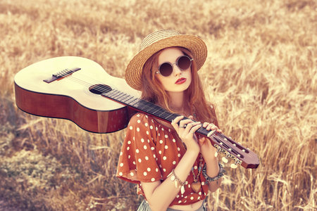 Happy hippie girl stands in a wheat field with her guitar. Spirit of freedom and independence.