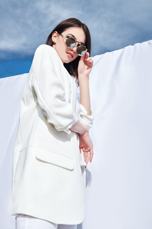 Fashion shot. Beautiful young woman model posing outdoor in white clothes among white fabrics...
