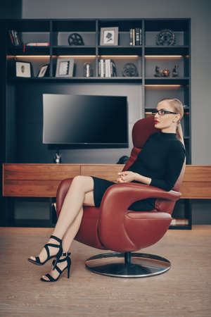 Portrait of a stunning fashionable woman sitting in a luxurious leather chair. Business, elegant businesswoman. Modern interior, furniture.の写真素材