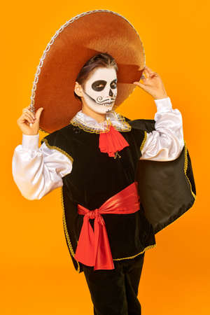 Portrait of a handsome boy with sugar skull makeup over bright yellow background. Halloween. Dia de los muertos. Day of the dead. Copy space.の写真素材