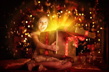 Cute little girl sits with a gift box by a beautiful Christmas tree. Christmas and New Year concept.