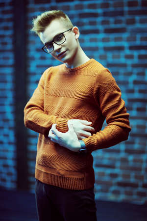 Portrait of a smart young guy in a pullover and glasses against a brick wall.の写真素材
