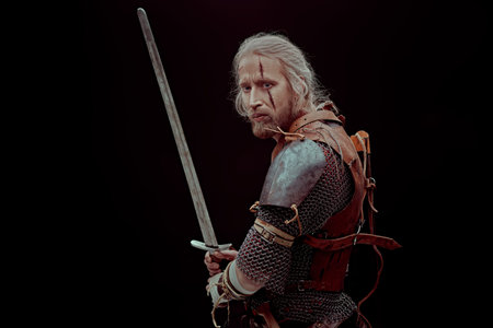 Portrait of a brave medieval warrior in armor with a sword on a black background. The Witcher man.