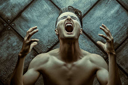 Pain. Art portrait of a naked muscular man who screams on a dark grunge background. Emotions.の写真素材