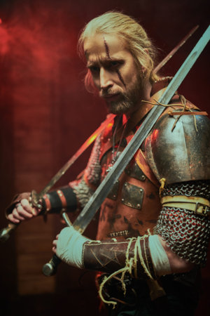 Portrait of a brave medieval warrior in armor with swords on a dark background. The Witcher man.