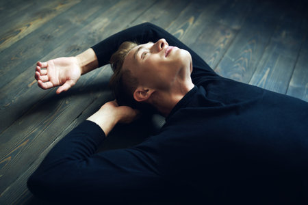 Male beauty, fashion. Portrait of a handsome young man in black clothes lying on a floor.