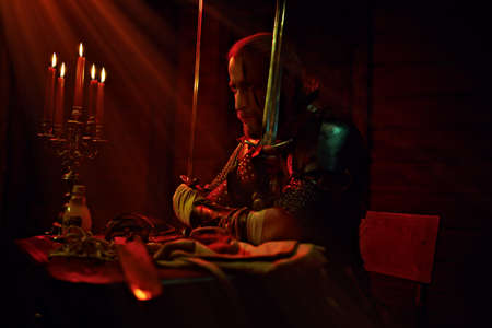 An experienced medieval warrior in armor and with a sword in a wooden house. Stage portrait. The Witcher man.の写真素材