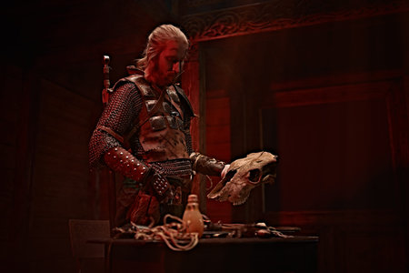 A Viking in armor holds an animal's skull in his hands, thinking in a tavern.