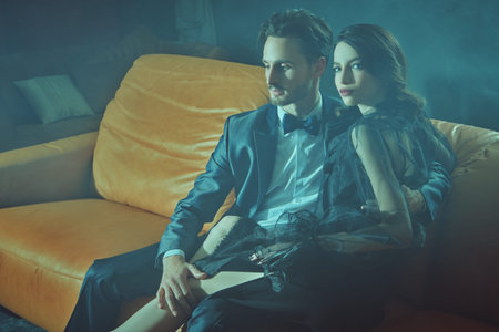 Beautiful elegant couple in fashionable evening clothes posing in haze in luxury apartment....