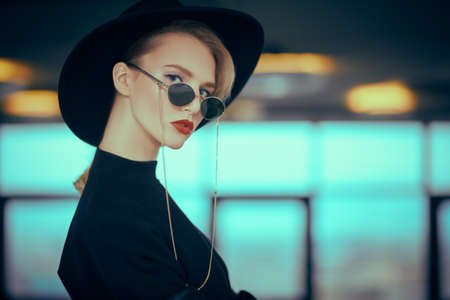 Fashionable young woman in black clothes and sunglasses in interiors. Beauty, fashion. Optics and eyewear.の写真素材