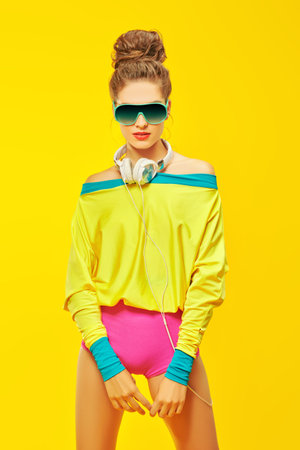 Colorful party girl posing in trendy vivid clothes and headphones on a yellow background. Disco...