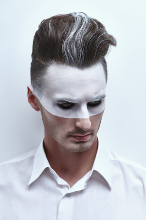 Fashion art portrait of a handsome man with white paint on his face and hair posing in white shirt...