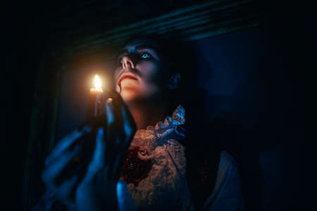 Close-up portrait of a mysterious vampire looking at a candle flame in the night. Halloween.の写真素材
