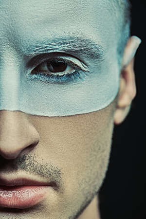 Close-up art portrait of a handsome man with white paint on his face on a black background. Male beauty, fashion. Hairstyle and cosmetics.の写真素材