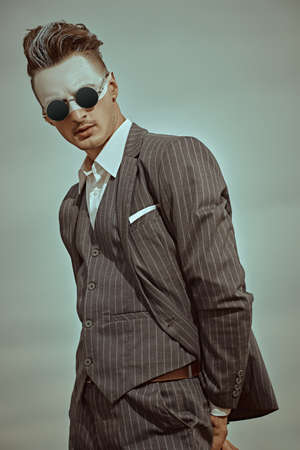 Men's fashion concept. Art portrait of a handsome man with white paint on his face posing in elegant suit and sunglasses against the cloudy sky. Body painting.の写真素材