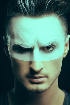 Art concept. Portrait of a brutal serious man frowning, white paint on his face and hair on a black...