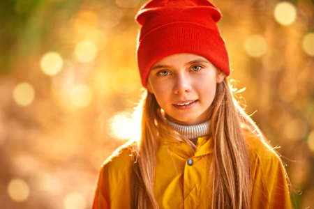 Cute child girl in red hat and yellow cloak looks at the camera and smiling. Autumn fashion for children.の写真素材