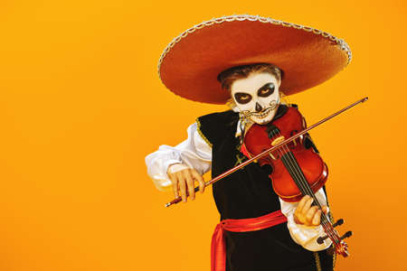 Handsome boy with sugar skull makeup plays the violin over bright yellow background. Halloween. Dia de los muertos. Day of the dead. Copy space.の写真素材
