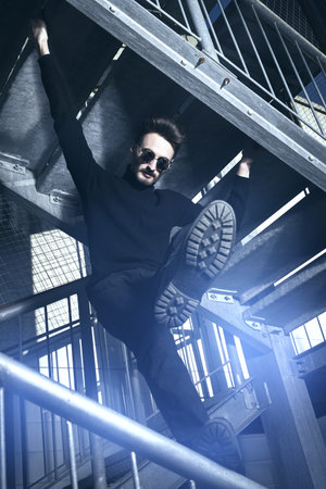 Portrait of a handsome courageous man in black clothes and black sunglasses posing on a metal...