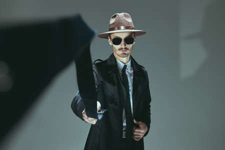 Male beauty, fashion. Portrait of a handsome man model in stylish clothes and sunglasses waving a belt at studio.の写真素材