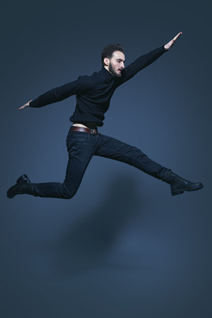 Full length portrait of a jumping young man in casual black clothes. Men's style. Studio shot on a...