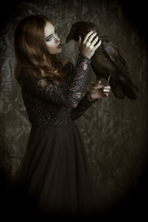 A witch in evening dress with a raven. Halloween. Celebration. Beauty and fashion. Dark force....