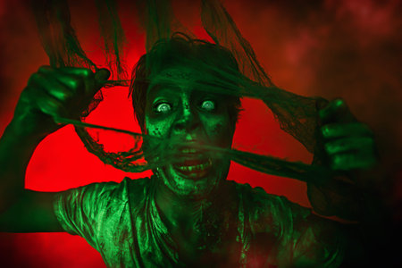 Halloween, horror movie. Portrait of a scary zombie boy teenager in smoke and red light.の写真素材