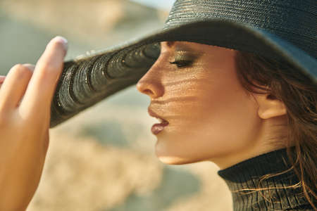 Close-up portrait of an elegant brunette woman in a wide-brimmed hat in the desert. Fashion shot. Summer vacation.の写真素材