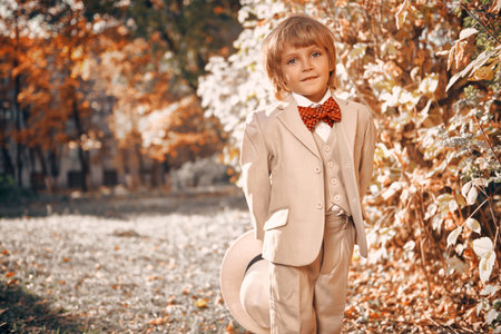 Portrait of a cute funny little boy in elegant white suit and white hat walking through a beautiful autumn park. Retro style. Children's fashion.の写真素材