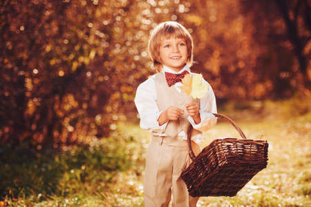 Portrait of a cute funny little boy in elegant white suit walking through a beautiful autumn park. Retro style. Children's fashion.の写真素材