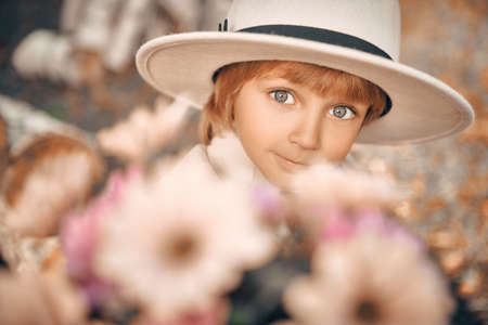 Close up portrait of happy little boy in hat surrounded by flowers. Retro style. Children's fashion.の写真素材